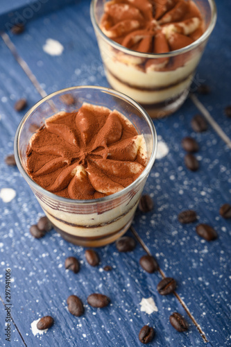 Tiramisu two glasses with coffee grains on a blue wooden background.Vertical photo