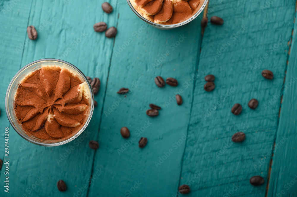 flat lay, Tiramisu two glasses with grains of coffee on a green wooden background. flat lay, Tiramisu two glasses with grains of coffee on a green wooden background.