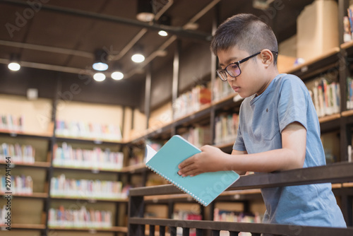 Asian boy student standing and reading a book at the library in the school.Students search for books in the bookshelf.Portrait Asian boy.