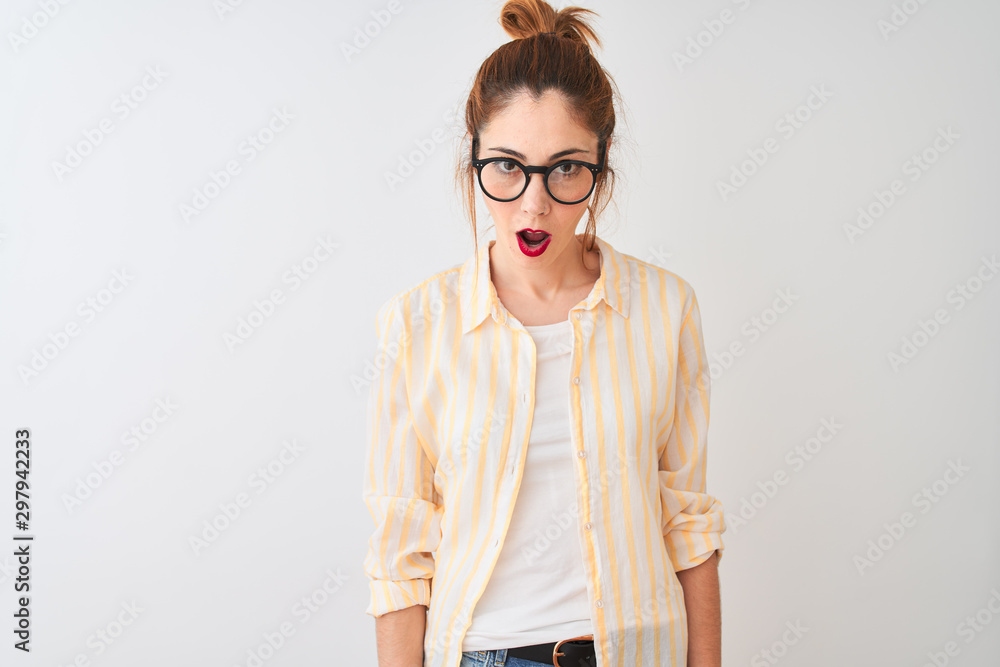 Redhead woman wearing striped shirt and glasses standing over isolated white background afraid and shocked with surprise expression, fear and excited face. Redhead woman wearing striped shirt and glasses standing over isolated white background afraid and shocked with surprise expression, fear and excited face.
