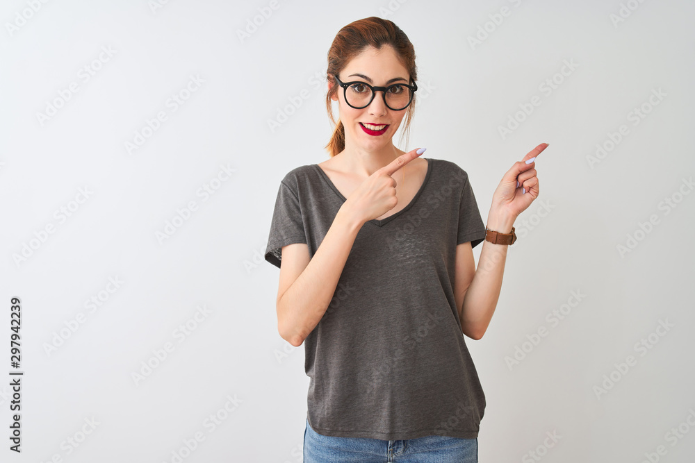 Redhead woman wearing casual t-shirt and glasses standing over isolated white background smiling and looking at the camera pointing with two hands and fingers to the side.