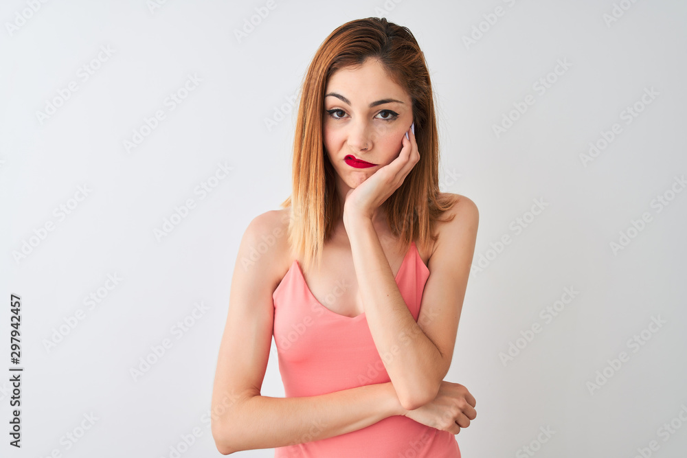 Beautiful redhead woman wearing casual pink t-shirt standing over isolated white background thinking looking tired and bored with depression problems with crossed arms. Beautiful redhead woman wearing casual pink t-shirt standing over isolated white background thinking looking tired and bored with depression problems with crossed arms.