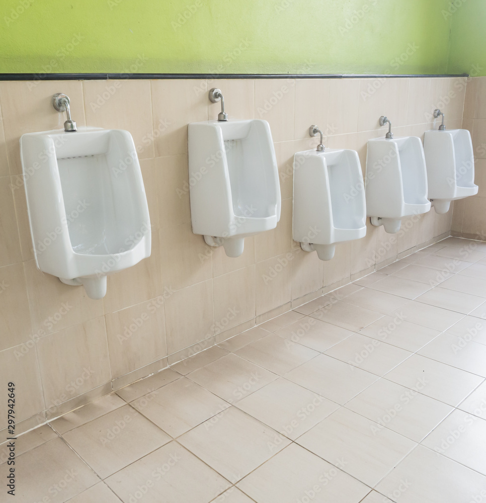 Empty row of outdoor urinals men public toilet and green wall