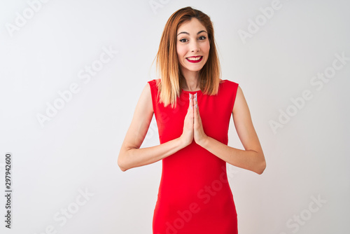 Redhead businesswoman wearing elegant red dress standing over isolated white background praying with hands together asking for forgiveness smiling confident.