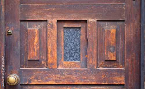 Weathered aged oiled brown timber door panel with a window pane and an ornamental door knob.