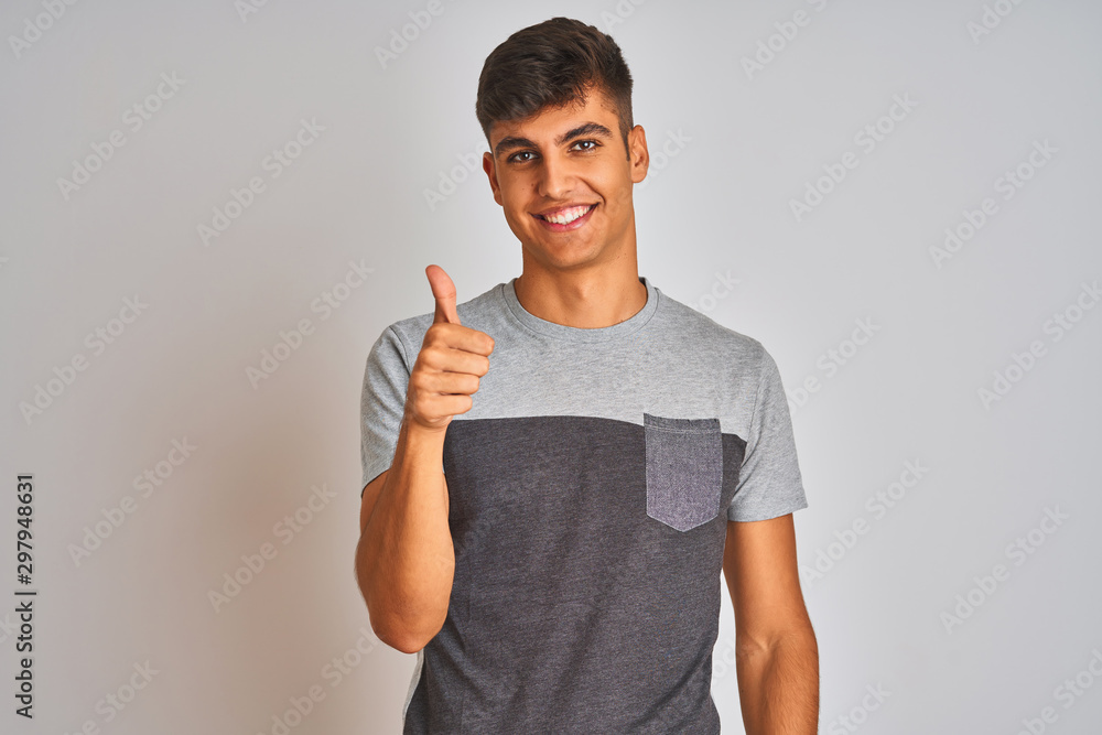 Young indian man wearing casual t-shirt standing over isolated white background doing happy thumbs up gesture with hand. Approving expression looking at the camera with showing success. Young indian man wearing casual t-shirt standing over isolated white background doing happy thumbs up gesture with hand. Approving expression looking at the camera with showing success.
