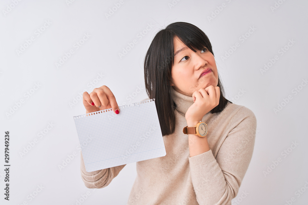 Young beautiful chinese woman holding notebook over isolated white background serious face thinking about question, very confused idea Young beautiful chinese woman holding notebook over isolated white background serious face thinking about question, very confused idea