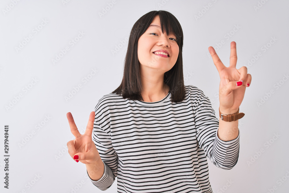 Young beautiful chinese woman wearing black striped t-shirt over isolated white background smiling looking to the camera showing fingers doing victory sign. Number two. Young beautiful chinese woman wearing black striped t-shirt over isolated white background smiling looking to the camera showing fingers doing victory sign. Number two.