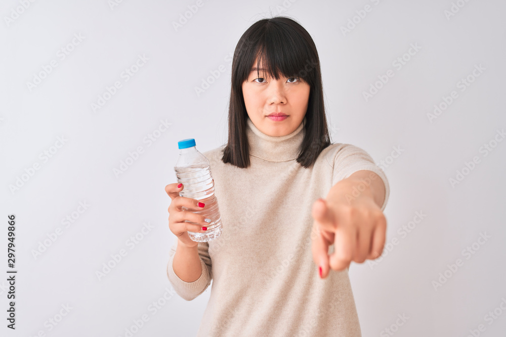 Young beautiful Chinese woman holding bottle of water over isolated white background pointing with finger to the camera and to you, hand sign, positive and confident gesture from the front Young beautiful Chinese woman holding bottle of water over isolated white background pointing with finger to the camera and to you, hand sign, positive and confident gesture from the front