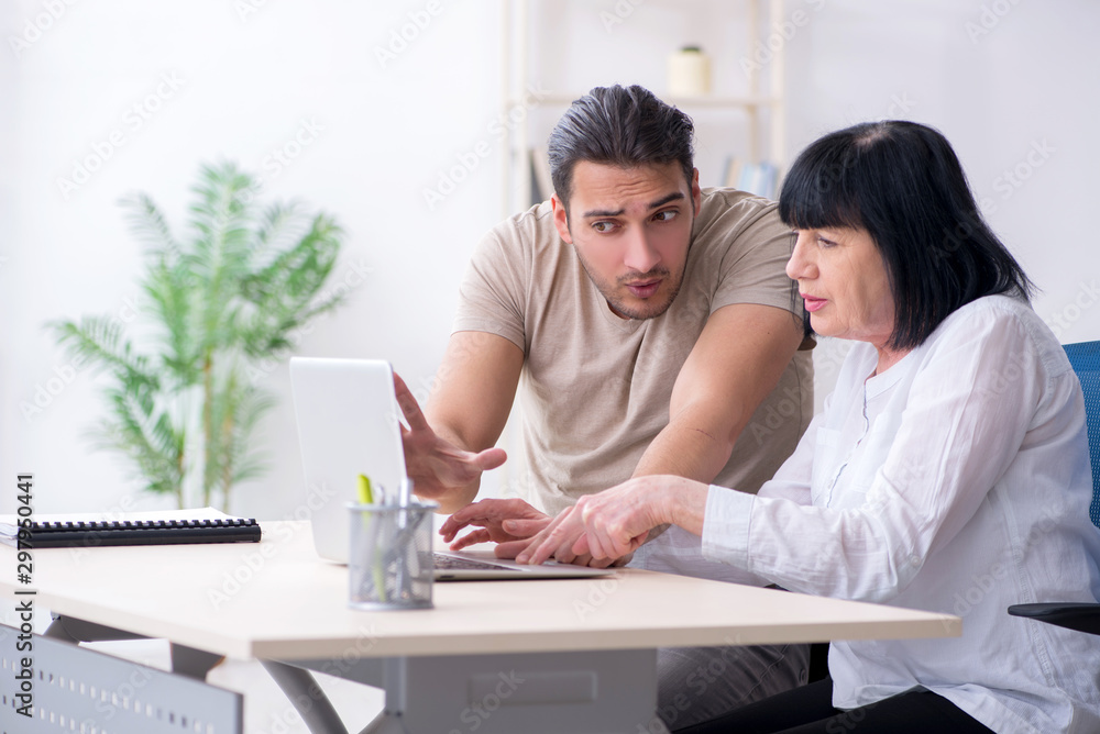 Young male employee explaining to old female colleague how to us Young male employee explaining to old female colleague how to us
