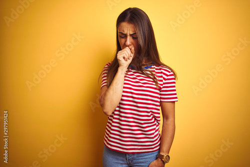 Young beautiful woman wearing striped t-shirt standing over isolated yellow background feeling unwell and coughing as symptom for cold or bronchitis. Healthcare concept.