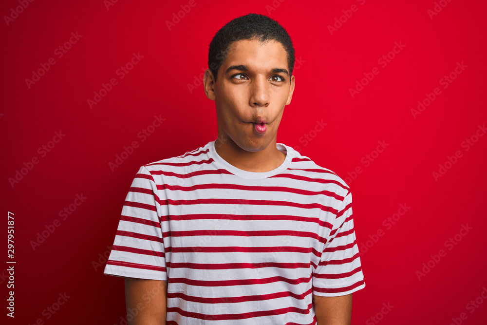 Young handsome arab man wearing striped t-shirt over isolated red background making fish face with lips, crazy and comical gesture. Funny expression. Young handsome arab man wearing striped t-shirt over isolated red background making fish face with lips, crazy and comical gesture. Funny expression.