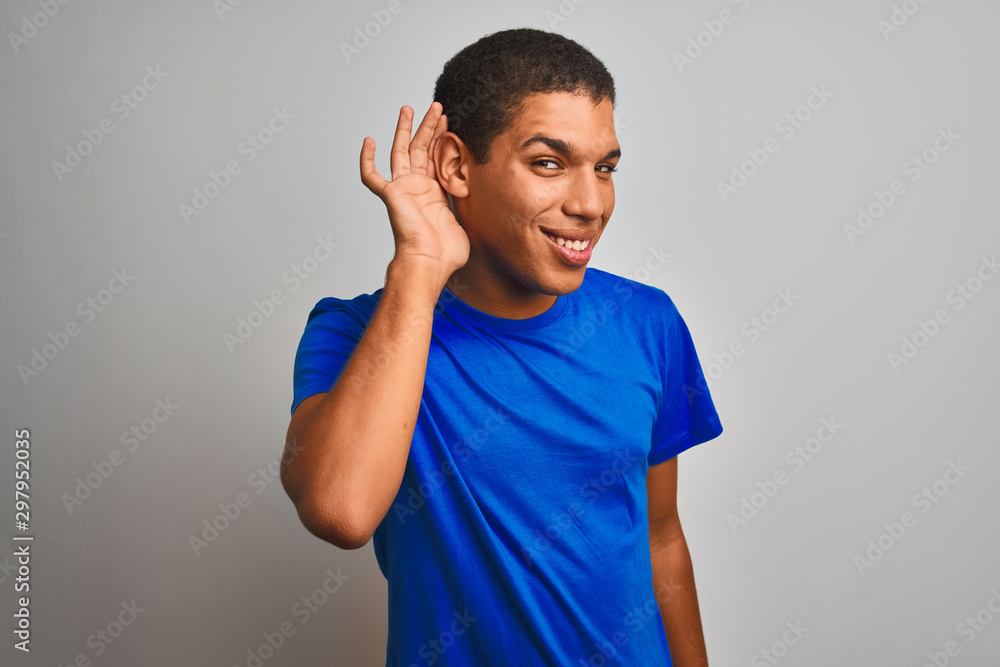 Young handsome arab man wearing blue t-shirt standing over isolated white background smiling with hand over ear listening an hearing to rumor or gossip. Deafness concept. Young handsome arab man wearing blue t-shirt standing over isolated white background smiling with hand over ear listening an hearing to rumor or gossip. Deafness concept.