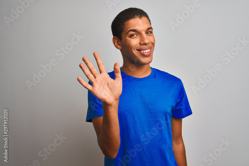 Young handsome arab man wearing blue t-shirt standing over isolated white background showing and pointing up with fingers number five while smiling confident and happy. © Krakenimages.com