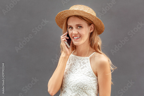 Freestyle. Young woman in hat standing isolated on wall talking on smartphone looking camera joyful close-up © Viktoriia