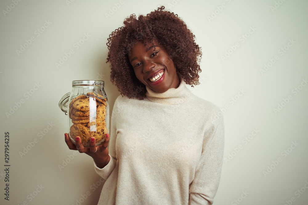 Young african afro woman holding jar of cookies standing over isolated white background with a happy face standing and smiling with a confident smile showing teeth Young african afro woman holding jar of cookies standing over isolated white background with a happy face standing and smiling with a confident smile showing teeth