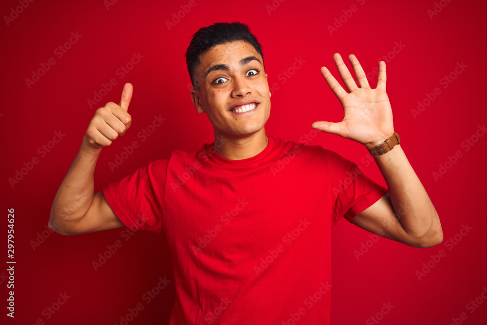 Naklejka premium Young brazilian man wearing t-shirt standing over isolated red background showing and pointing up with fingers number six while smiling confident and happy.