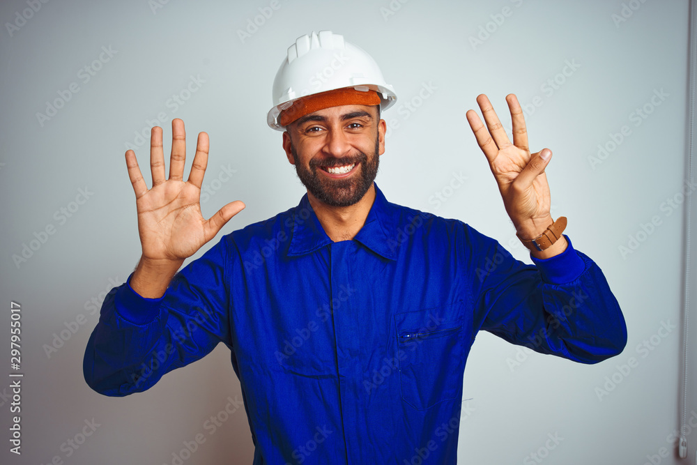 Handsome indian worker man wearing uniform and helmet over isolated white background showing and pointing up with fingers number eight while smiling confident and happy.