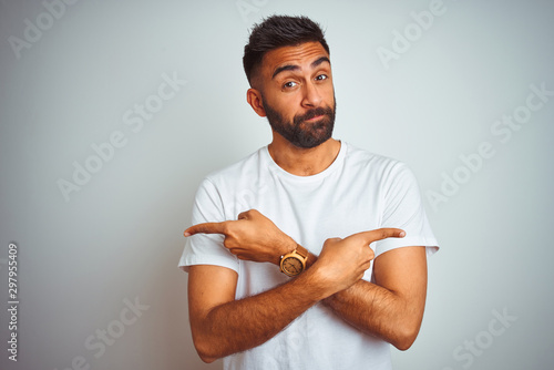 Young indian man wearing t-shirt standing over isolated white background Pointing to both sides with fingers, different direction disagree photo