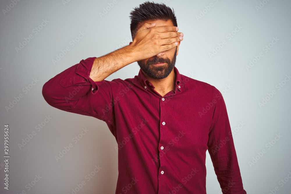 Young indian man wearing red elegant shirt standing over isolated grey background covering eyes with hand, looking serious and sad. Sightless, hiding and rejection concept Young indian man wearing red elegant shirt standing over isolated grey background covering eyes with hand, looking serious and sad. Sightless, hiding and rejection concept