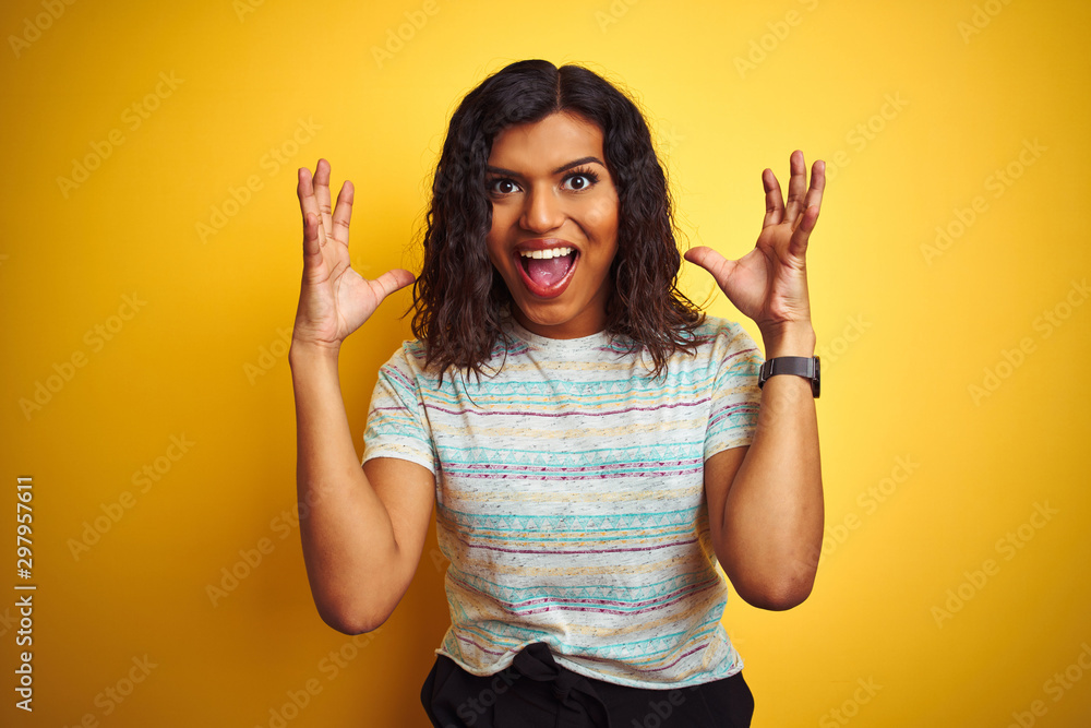 Beautiful transsexual transgender woman wearing t-shirt over isolated yellow background celebrating crazy and amazed for success with arms raised and open eyes screaming excited. Winner concept Beautiful transsexual transgender woman wearing t-shirt over isolated yellow background celebrating crazy and amazed for success with arms raised and open eyes screaming excited. Winner concept