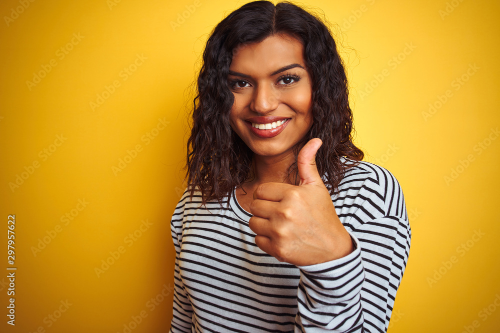 Transsexual transgender woman wearing striped t-shirt over isolated yellow background happy with big smile doing ok sign, thumb up with fingers, excellent sign Transsexual transgender woman wearing striped t-shirt over isolated yellow background happy with big smile doing ok sign, thumb up with fingers, excellent sign
