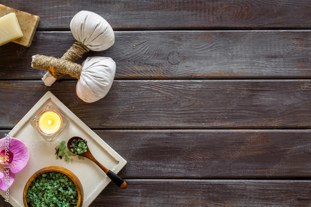 Massage table with thai herbal balls, candles and orchids on dark wooden background top view frame copy space Massage table with thai herbal balls, candles and orchids on dark wooden background top view frame copy space