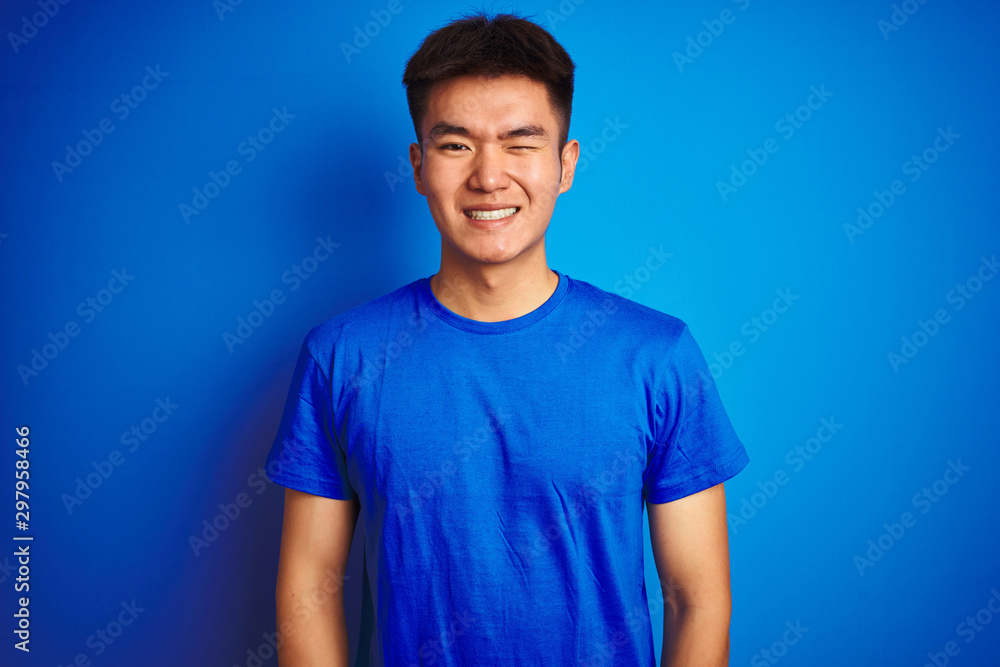 Young asian chinese man wearing t-shirt standing over isolated blue background winking looking at the camera with sexy expression, cheerful and happy face. Young asian chinese man wearing t-shirt standing over isolated blue background winking looking at the camera with sexy expression, cheerful and happy face.