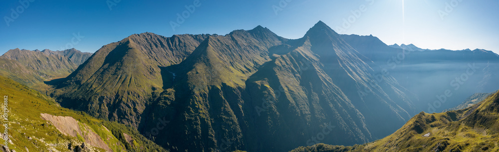 Panoramic drone footage; panoramic view of mountain ridges in early summer morning; green alpine slopes and stony peaks; natural highland landscape; shadows and silhouettes of Pseashkho peak