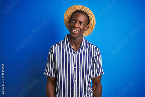 African american man wearing striped shirt and summer hat over isolated blue background looking away to side with smile on face, natural expression. Laughing confident. © Krakenimages.com