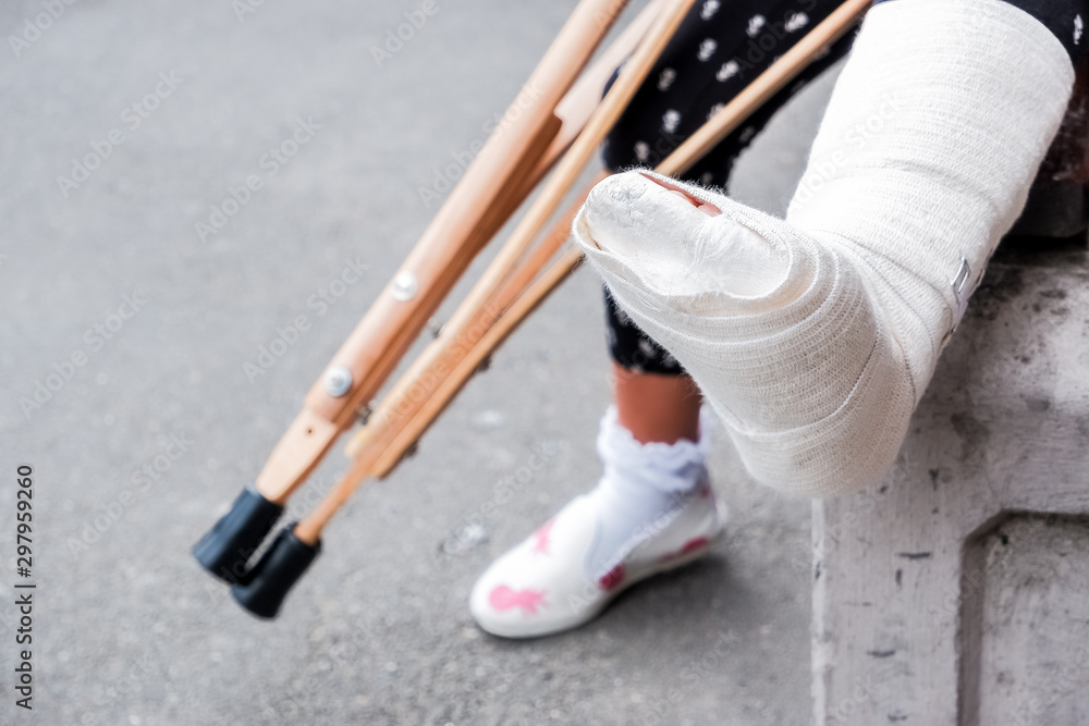 unrecognizable girl sits on the street on a bench with a broken leg and  crutches.disabled girl with crutches.an accident while jumping on a  trampoline. An ankle fracture. Photos | Adobe Stock