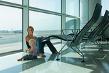 Mother with little kid wait for boarding to plane flight in airport transit hall. Baby look through the window at flying airplane. Active family lifestyle, travel by air with child on summer vacation.