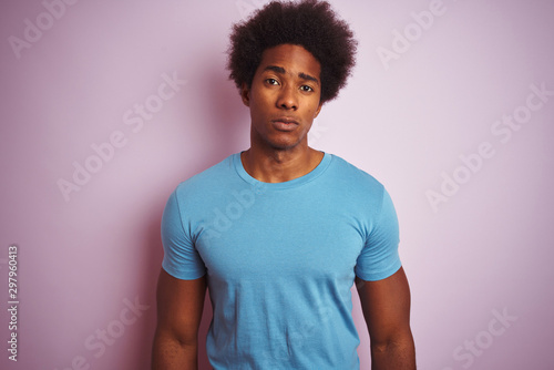 African american man with afro hair wearing blue t-shirt standing over isolated pink background Relaxed with serious expression on face. Simple and natural looking at the camera.