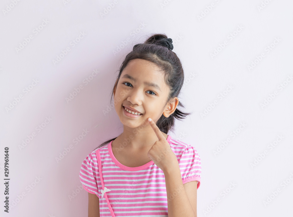 The child with black hair is smiling and pointing to her face. The child with black hair is smiling and pointing to her face.