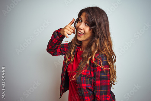 Young beautiful woman wearing red t-shirt and jacket standing over white isolated background smiling doing phone gesture with hand and fingers like talking on the telephone. Communicating concepts.