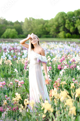 Young girl wearing white dress standing near irises on garden. photo