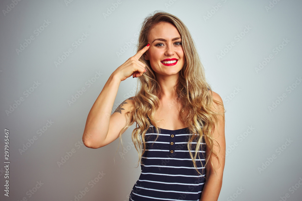 Young beautiful woman wearing stripes t-shirt standing over white isolated background Smiling pointing to head with one finger, great idea or thought, good memory