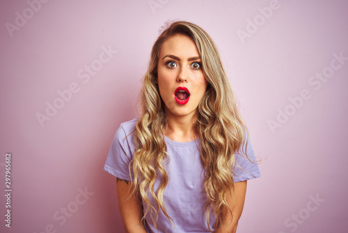 Young beautiful woman wearing purple t-shirt standing over pink isolated background afraid and shocked with surprise expression, fear and excited face.