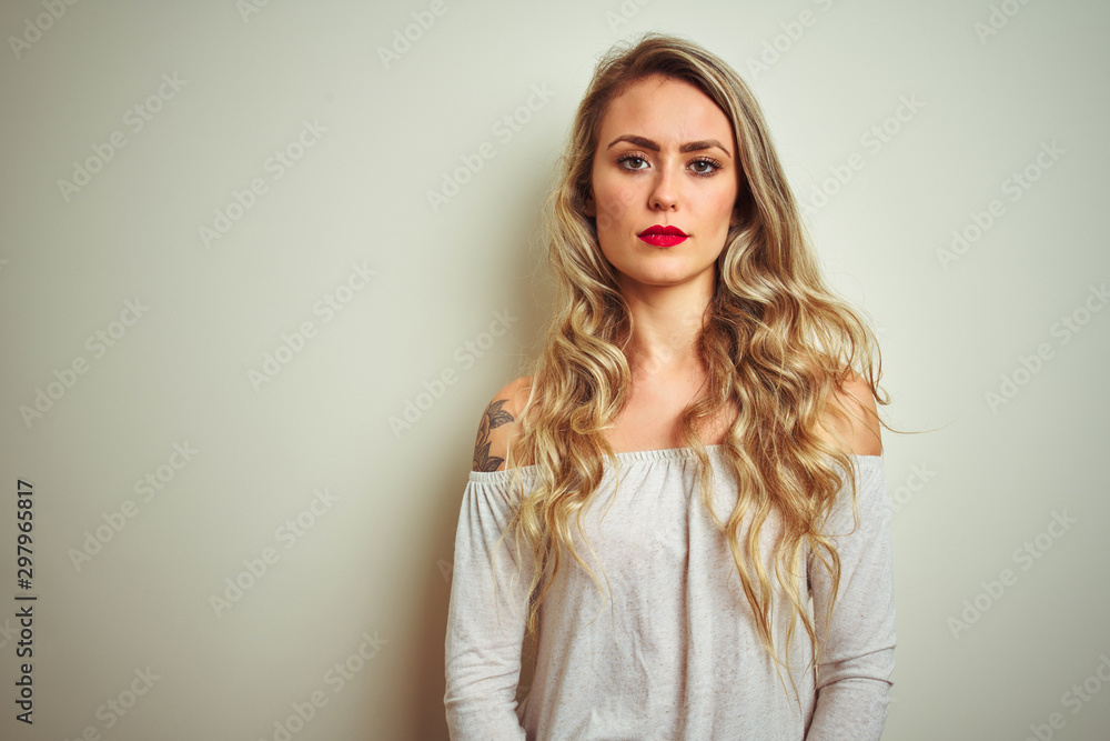 Young beautiful woman standing over white isolated background with serious expression on face. Simple and natural looking at the camera. Young beautiful woman standing over white isolated background with serious expression on face. Simple and natural looking at the camera.
