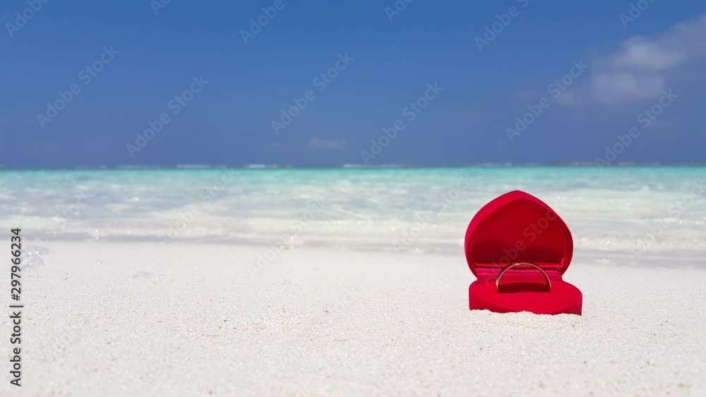 An engagement ring in a heart shaped case on a beautiful white sand beach with waves and clear blue sky in background in New Caledonia, France - Closeup shot An engagement ring in a heart shaped case on a beautiful white sand beach with waves and clear blue sky in background in New Caledonia, France - Closeup shot