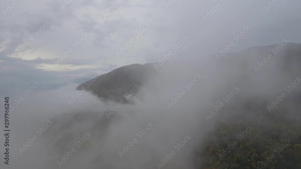 A drone flys through the clouds and mists on a foogy grey sky day above a autumn fall alpine forest in the Alpine mountains of france and Switzerland. A drone flys through the clouds and mists on a foogy grey sky day above a autumn fall alpine forest in the Alpine mountains of france and Switzerland.