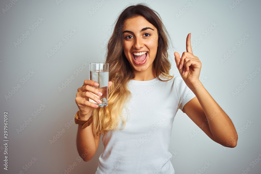 Young beautiful woman drinking a glass of water over white isolated background surprised with an idea or question pointing finger with happy face, number one Young beautiful woman drinking a glass of water over white isolated background surprised with an idea or question pointing finger with happy face, number one