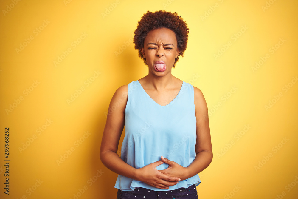 Beautiful african american woman wearing elegant shirt over isolated yellow background sticking tongue out happy with funny expression. Emotion concept. Beautiful african american woman wearing elegant shirt over isolated yellow background sticking tongue out happy with funny expression. Emotion concept.