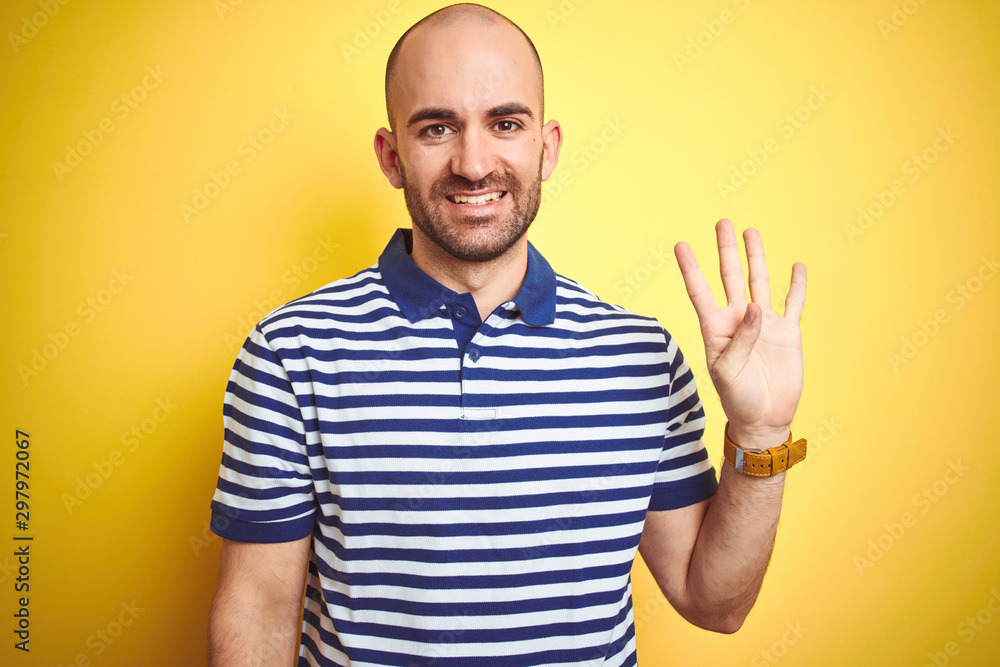 Young bald man with beard wearing casual striped blue t-shirt over yellow isolated background showing and pointing up with fingers number four while smiling confident and happy. Young bald man with beard wearing casual striped blue t-shirt over yellow isolated background showing and pointing up with fingers number four while smiling confident and happy.