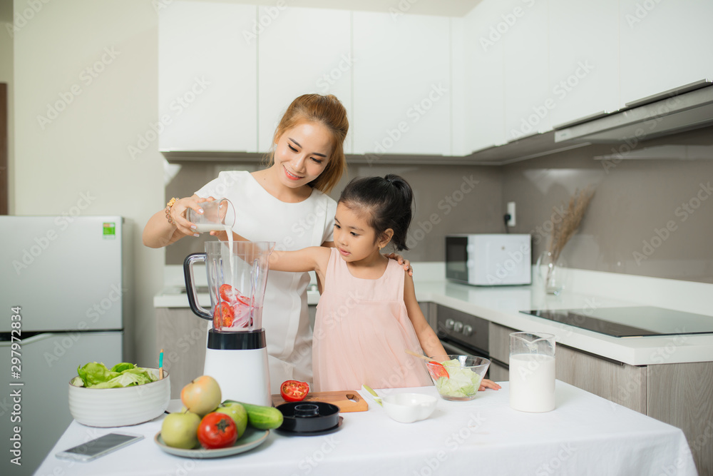 Young Asian mother and daughter making freshly squeezed tomato smoothies, daughter is very happy