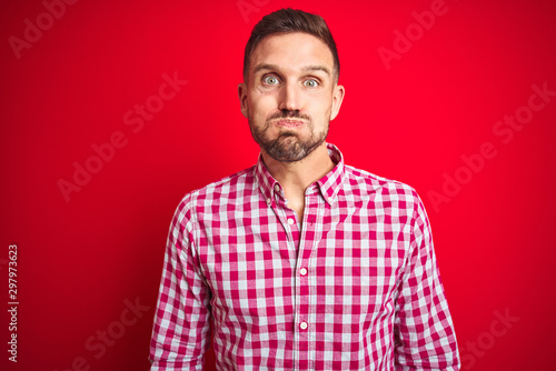 Young handsome man over red isolated background puffing cheeks with funny face. Mouth inflated with air, crazy expression.