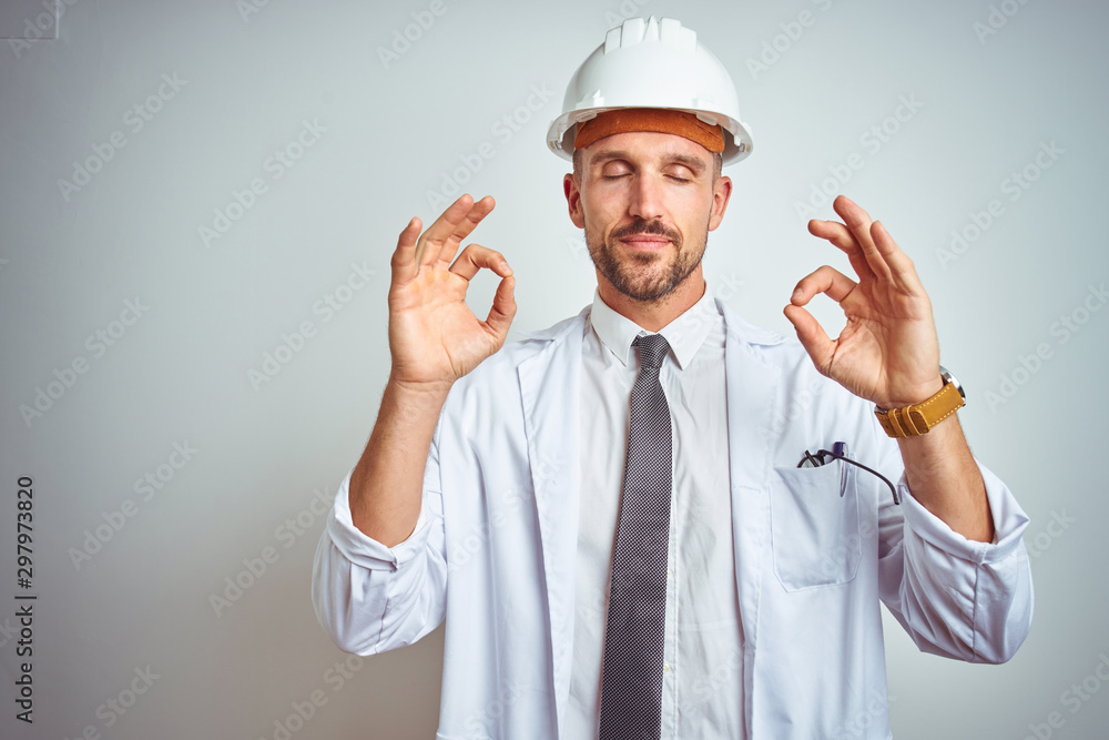 Young handsome engineer man wearing safety helmet over isolated background relax and smiling with eyes closed doing meditation gesture with fingers. Yoga concept.