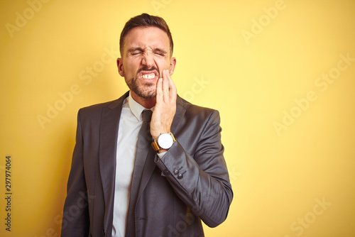 Young handsome business man over yellow isolated background touching mouth with hand with painful expression because of toothache or dental illness on teeth. Dentist concept.