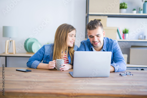 Young couple relaxing drinking a coffee and using the computer laptop around cardboard boxes, very happy moving to a new house