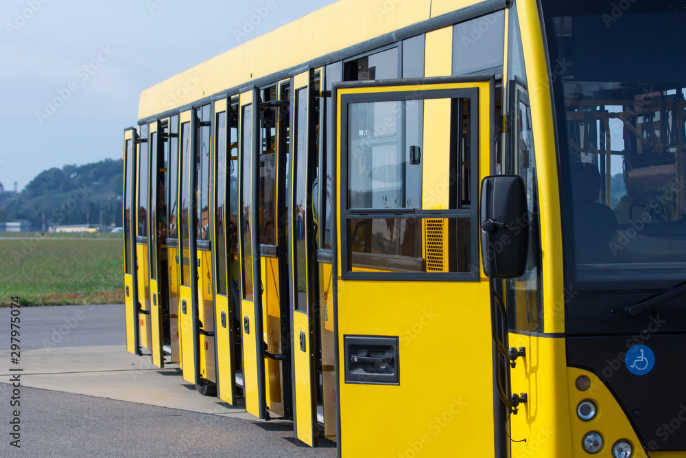 Yellow passenger bus with open doors waiting for passengers to transport to the plane at the airport.